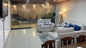 A modern living room with a glass wall, a sofa set, a coffee table, and a dining area.