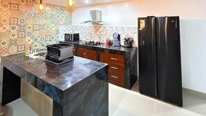A modern kitchen with a marble island, wooden ceiling, patterned backsplash, and a black refrigerator.