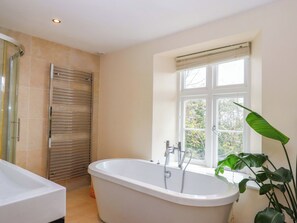 Un baño con una bañera independiente, un perchero y una ventana con vista a árboles.
