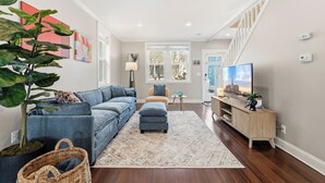 A modern living room with a sectional sofa, a coffee table, a TV, and a staircase leading upstairs. - Spacious and furnished 4-bedroom in beautiful Washington, DC. (Washington)