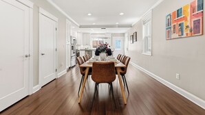 A dining area with a long table, chairs, and a kitchen in the background. - Spacious and furnished 4-bedroom in beautiful Washington, DC. (Washington)