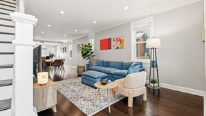 A modern living room with a blue sofa, a beige armchair, a patterned rug, and a dining area with a table and chairs. - Spacious and furnished 4-bedroom in beautiful Washington, DC. (Washington)