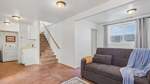 Un salon comprenant un canapé, un tapis, un escalier et un coin cuisine.