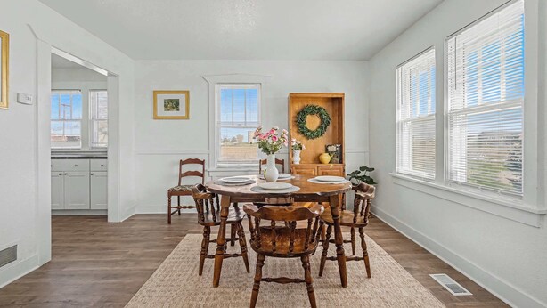 Un coin repas avec une table en bois, des chaises, un tapis et une couronne décorative accrochée au mur.