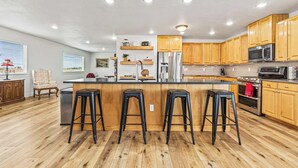 A modern kitchen with wooden cabinets, a stainless steel refrigerator, a microwave, and a bar area with stools. - Big Foot Ranch Retreat – Spacious Idaho Home w/ View (Melba)