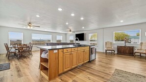 A spacious kitchen with wooden cabinets, a central island, and a dining area with chairs. - Big Foot Ranch Retreat – Spacious Idaho Home w/ View (Melba)