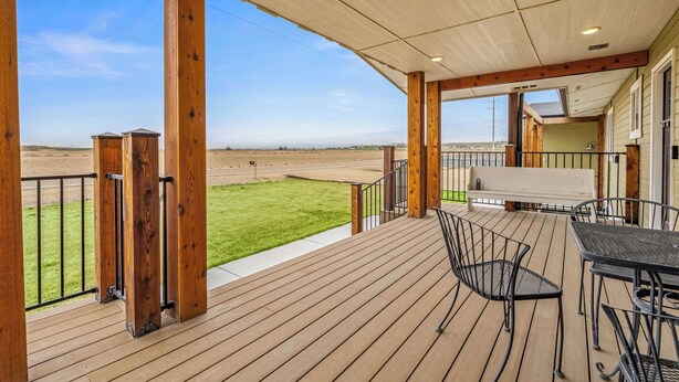 A covered outdoor deck with a view of a grassy field, a bench, and a table with chairs. - Big Foot Ranch Retreat – Spacious Idaho Home w/ View (Melba)