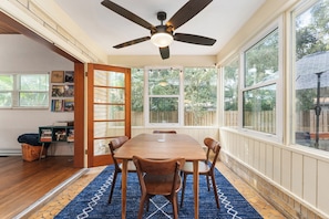A dining area with a wooden table, chairs, a ceiling fan, and large windows.