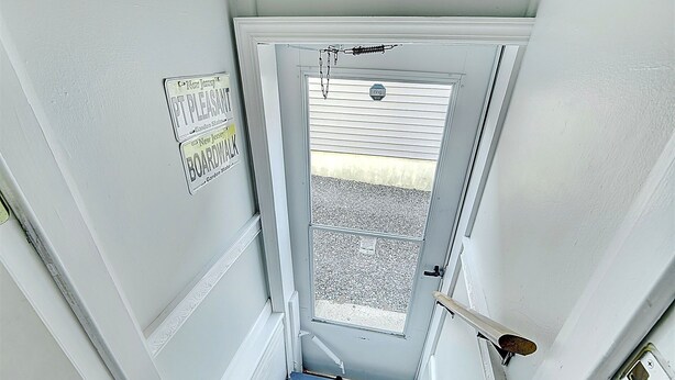 Una escalera estrecha que conduce a una puerta con ventanal, timbre y un letrero que indica un paseo marítimo.