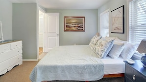 Un dormitorio con cama, cómoda, mesita de noche, lámpara y dos cuadros en la pared.