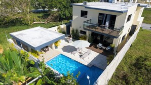 Uma casa moderna de dois andares com terraço no telhado, piscina e jardim.