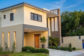 A modern two-story house with a flat roof, large windows, and a stone accent wall. - Villa Shorys: Free Electricity | 12Pax | Pool+Jacuzzi | A/C | Covered Parking (Punta Cana)