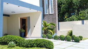 Um edifício moderno com telhado plano, entrada ampla e um jardim bem cuidado com diversas plantas.