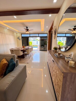 A modern living room with a sofa, dining area, and a large mirror. - Villa Shorys: Free Electricity | 12Pax | Pool+Jacuzzi | A/C | Covered Parking (Punta Cana)