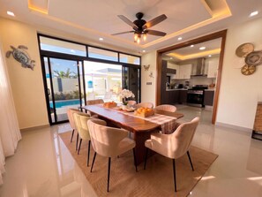 A modern dining area with a wooden table, cushioned chairs, and a view of the outdoor pool. - Villa Shorys: Free Electricity | 12Pax | Pool+Jacuzzi | A/C | Covered Parking (Punta Cana)