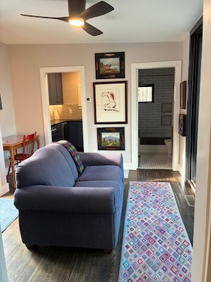 Un salon avec un canapé, un tapis à motifs et des œuvres d’art encadrées accrochées au mur.