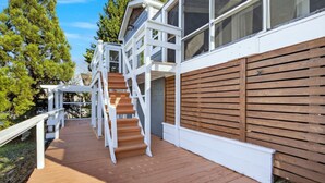 Une terrasse en bois avec un escalier menant à un bâtiment blanc doté de grandes fenêtres.