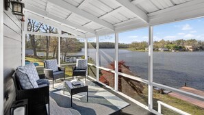 Un espace extérieur abrité, aménagé avec des meubles en osier, offrant une vue sur un lac et doté d’un mur extérieur blanc.