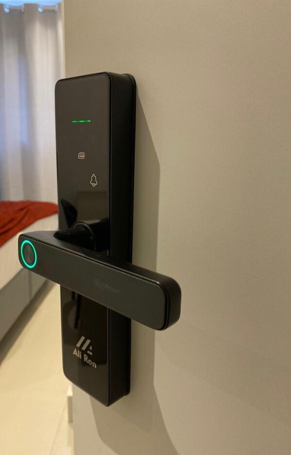 Cerradura electrónica fijada a la pared con luz indicadora verde, una ranura para llave y el nombre de marca 'Ali Ron'.