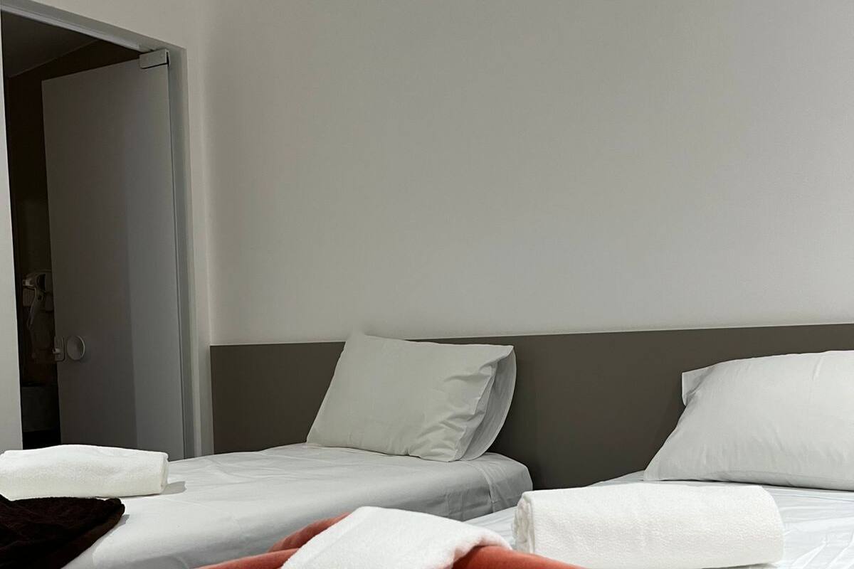 Une chambre d’hôtel avec deux lits, du linge de lit blanc et une couverture marron.