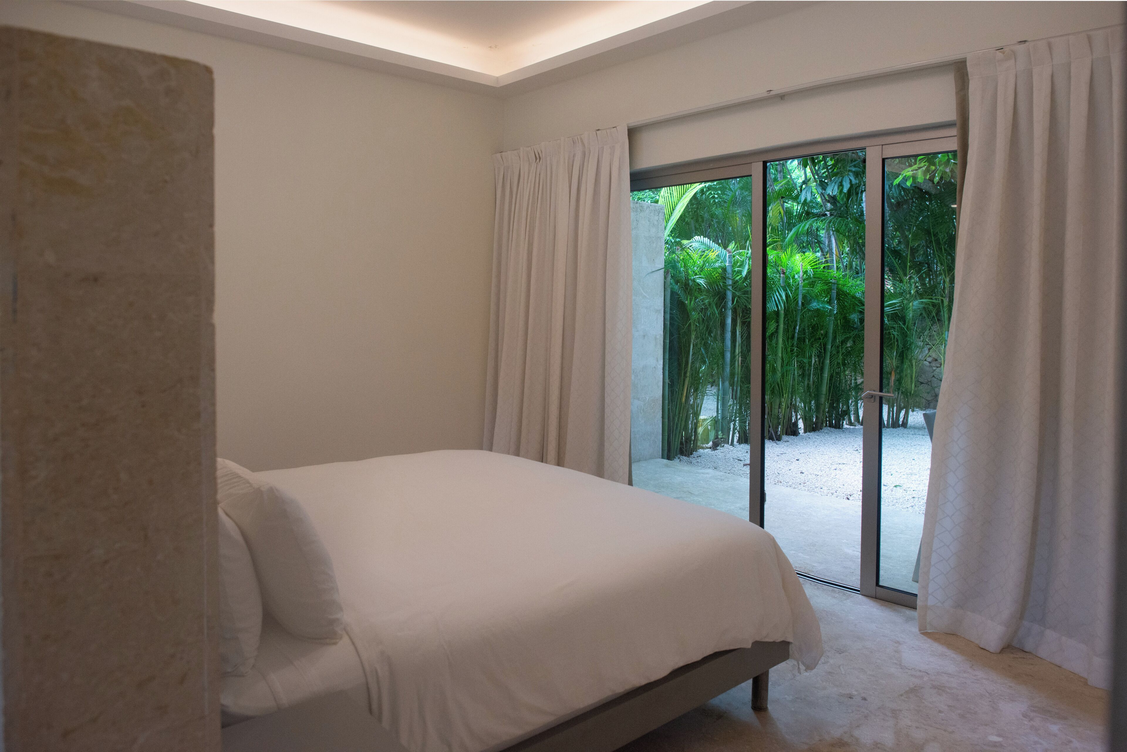 A bedroom with a bed, a large sliding glass door leading to a garden.