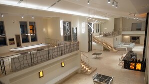Un espacio interior amplio con mesa de billar, varias zonas de estar y una escalera que conecta diferentes niveles.