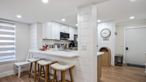 Una cocina moderna con armarios blancos, una isla central con taburetes, un microondas y un reloj en la pared.