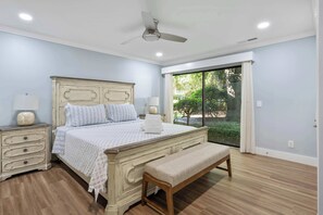 Ein Schlafzimmer mit Bett, Nachttischen, einer Bank, einem Deckenventilator und einem großen Fenster.