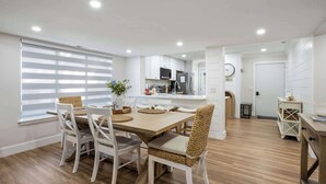 Una cocina moderna con muebles blancos, un comedor con mesa y sillas de madera, y vista al área de estar.