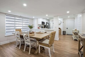Eine moderne Küche mit weißen Schränken, ein Essbereich mit Holztisch und -stühlen sowie Blick auf das Wohnzimmer.