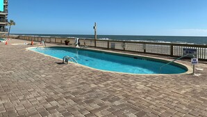 A swimming pool with a wooden deck, a lifeguard tower, and a view of the ocean.