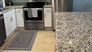 A modern kitchen with white cabinets, stainless steel appliances, a granite countertop, and a patterned rug.