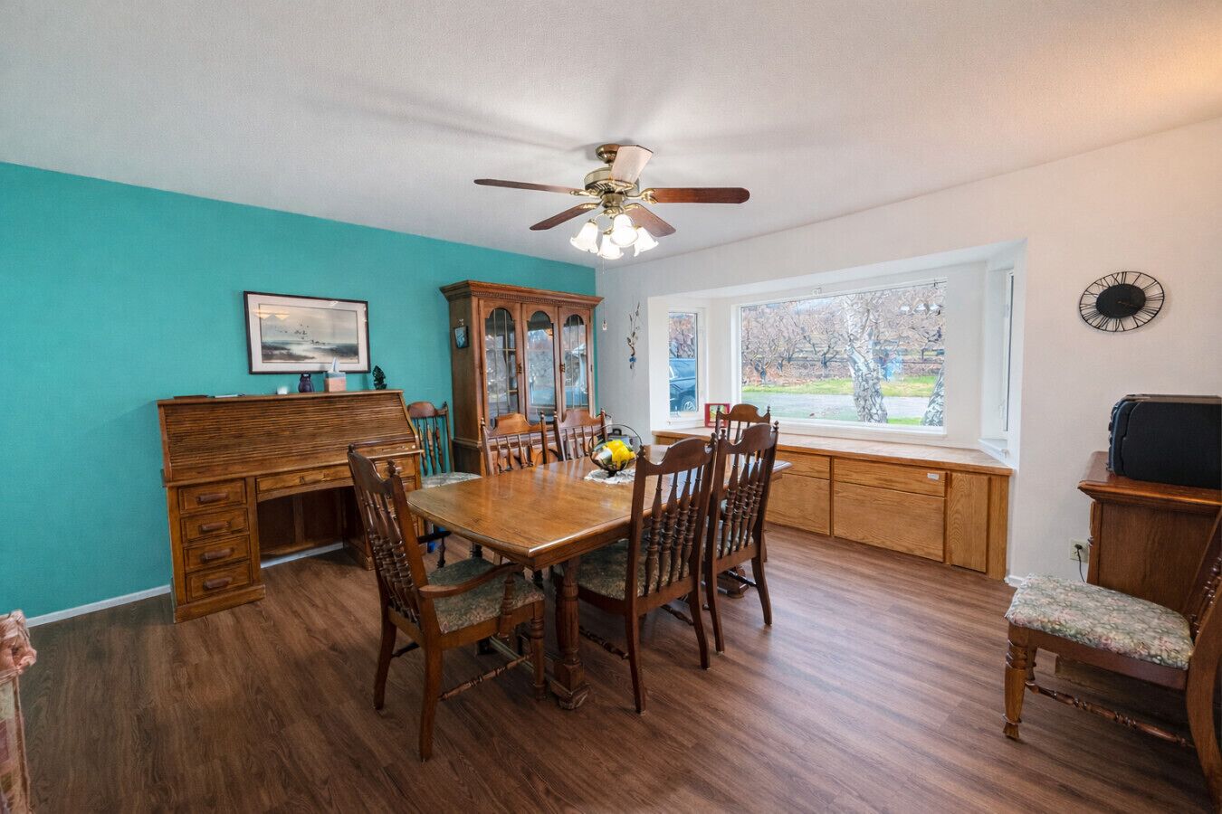A dining room with a wooden table, chairs, a piano, and a window with a view.