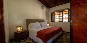 A bedroom with a bed, a nightstand, a window with wooden shutters, and a door.