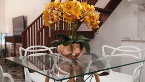 Et spiseområde med et glasbord, hvide stole og en vase med gule blomster.
