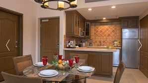 A modern kitchen with wooden cabinets, a stainless steel refrigerator, and a dining area with a glass table set for four. - Cozy 2 Bedroom Elite Suite at Villa del Palmar Loreto (Ensenada Blanca)