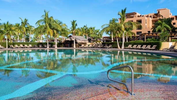 A swimming pool with lounge chairs and palm trees, surrounded by resort buildings. - Cozy 2 Bedroom Elite Suite at Villa del Palmar Loreto (Ensenada Blanca)