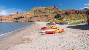 A beach with kayaks, a beach umbrella, and a mountain in the background. - Cozy 2 Bedroom Elite Suite at Villa del Palmar Loreto (Ensenada Blanca)