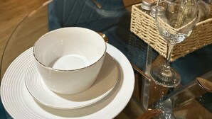 Una mesa de comedor con cuencos y platos blancos, un florero de vidrio con trigo seco, y un televisor al fondo.