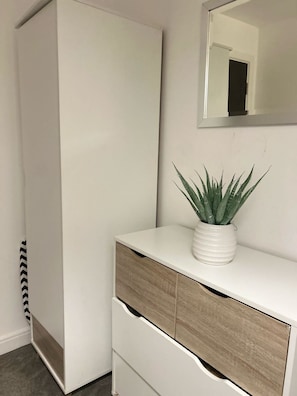 A white wardrobe with a mirror above it and a plant on a white dresser. - Super Comfy Condo in Central Manchester|Free Parking|Wi-Fi (Greater Manchester)