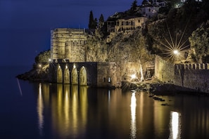 Ein historisches Steinhaus mit einer Brücke, umgeben von Bäumen und einem ruhigen Gewässer.