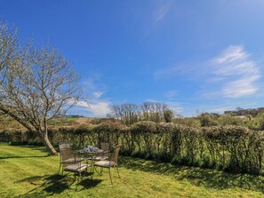 Ein Garten mit Tisch und Stühlen, umgeben von Bäumen und Hecken.