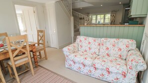 A dining area with a wooden table and chairs, a floral sofa, and a staircase leading to an upper level. - New Barn (Salisbury)
