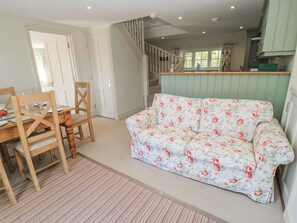 A dining area with a wooden table and chairs, a floral sofa, and a staircase leading to an upper level. - New Barn (Salisbury)