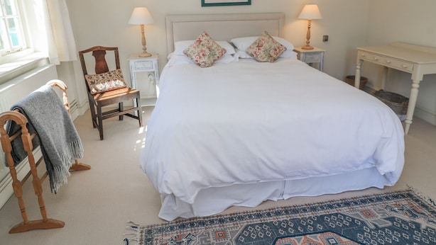A bedroom with a large bed, two bedside tables, a chair, a rug, and a framed picture on the wall. - New Barn (Salisbury)