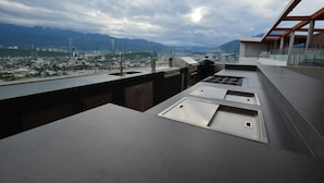 Cocina moderna con vistas a la ciudad, una parrilla y un amplio ventanal que domina un paisaje urbano y montañas.