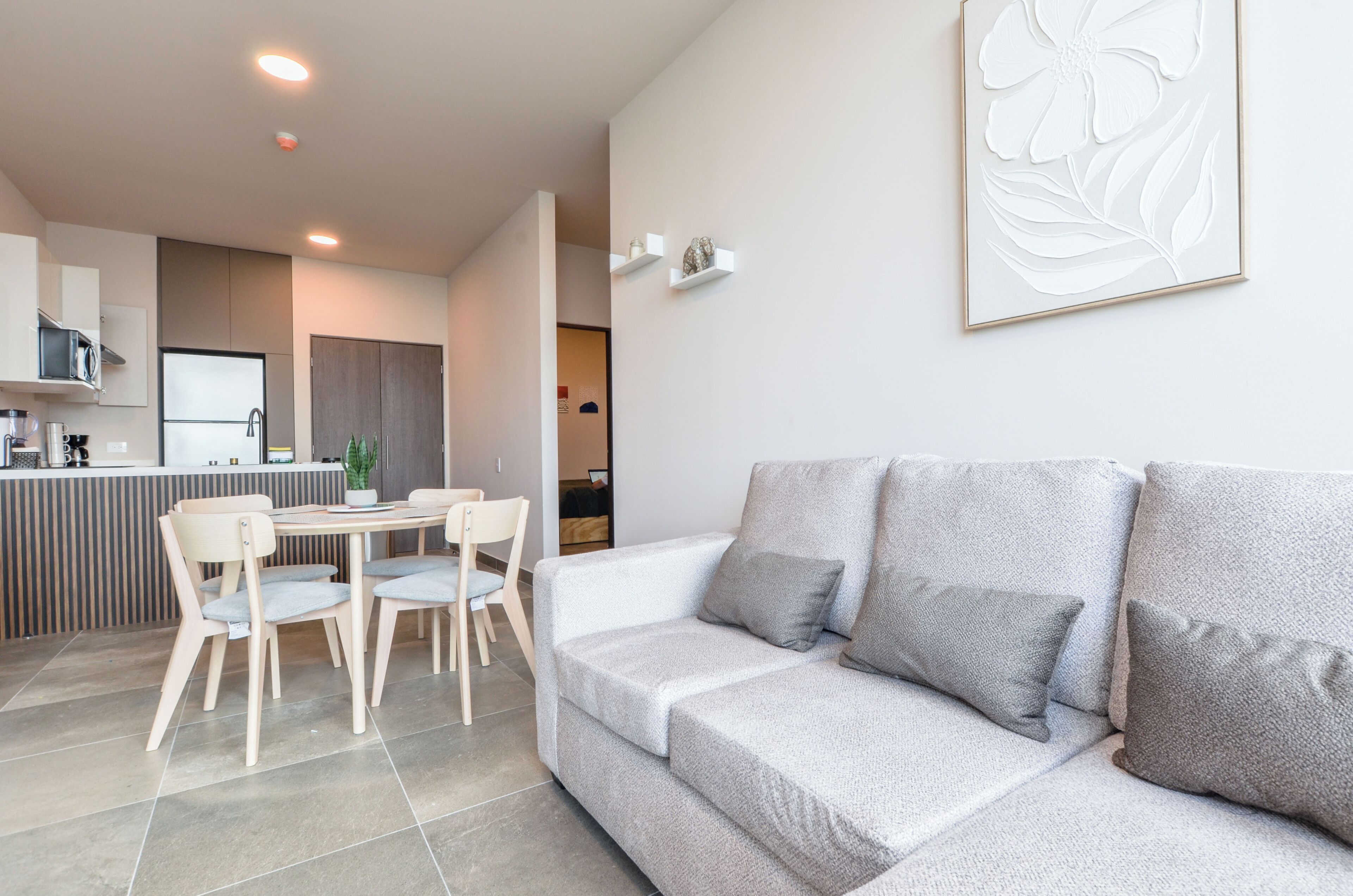 Un espace de vie moderne comprenant un canapé, des fauteuils, une table à manger et une cuisine en arrière-plan.