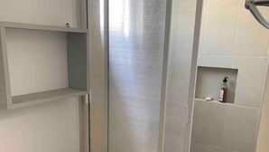 A bathroom with a toilet, a shower enclosure, and a shelf with toiletries. - House with heated pool and 5 min from the pacific ocean (Mazatlán)
