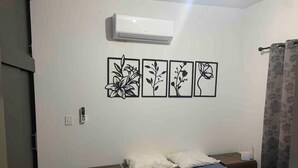 A bedroom with a bed, a bedside table, a wall-mounted air conditioner, and four framed floral artworks. - House with heated pool and 5 min from the pacific ocean (Mazatlán)