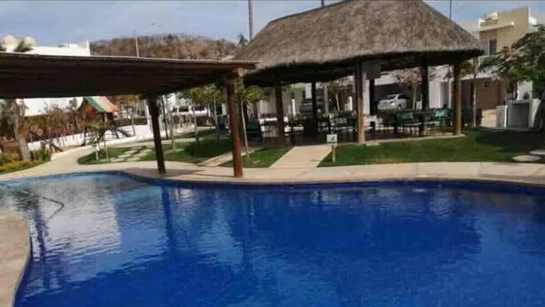 A clear blue swimming pool with a thatched-roof structure nearby. - House with heated pool and 5 min from the pacific ocean (Mazatlán)